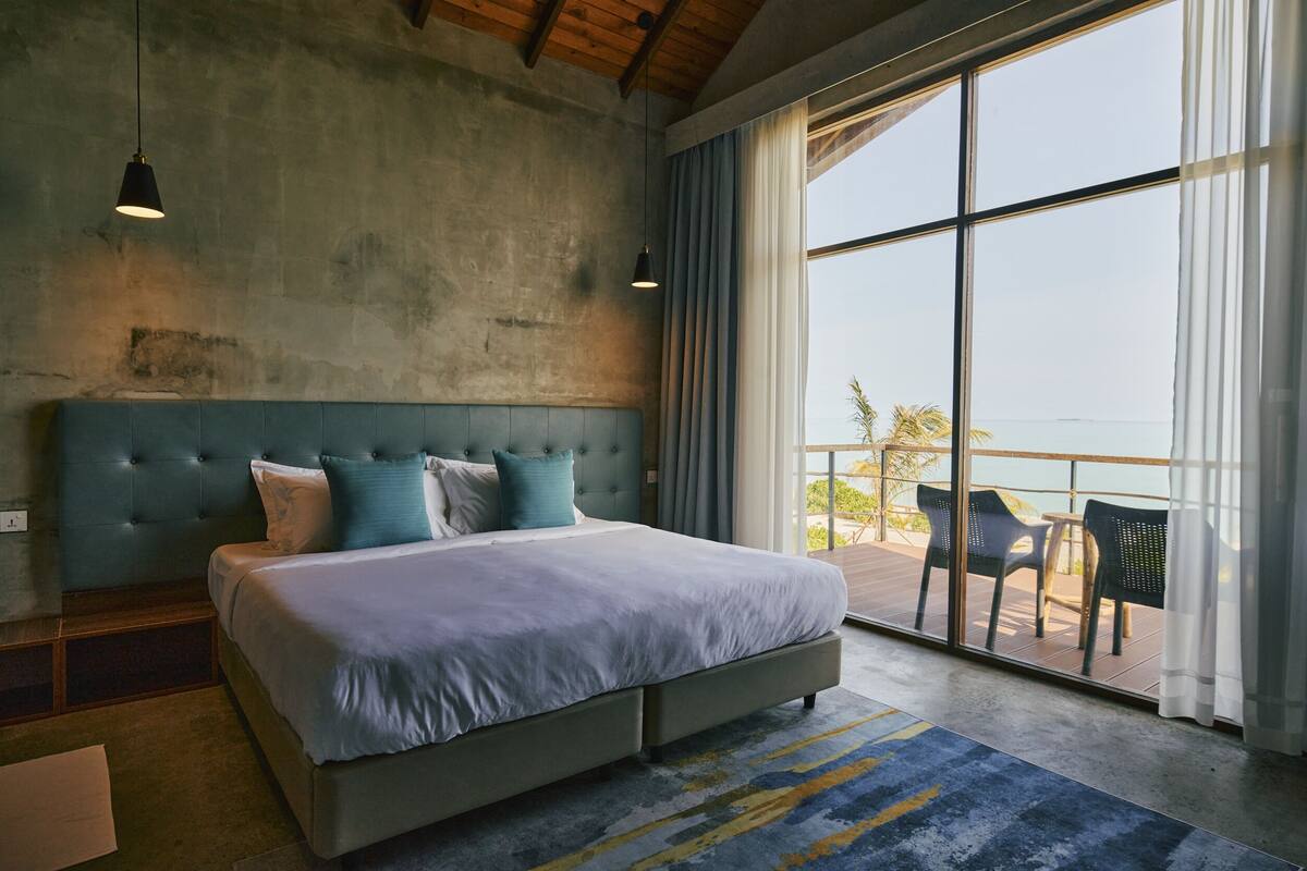 Quarto com cama grande, vista para o mar e varanda com cadeiras.