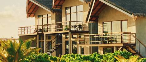 A beachfront property with a two-story structure, multiple balconies, and a thatched roof.