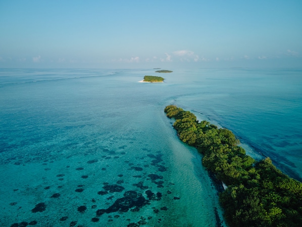 An aerial view of a tropical island with clear turquoise waters and a narrow strip of dense vegetation along the coastline. - Araaik Beach Village (Hoarafushi)