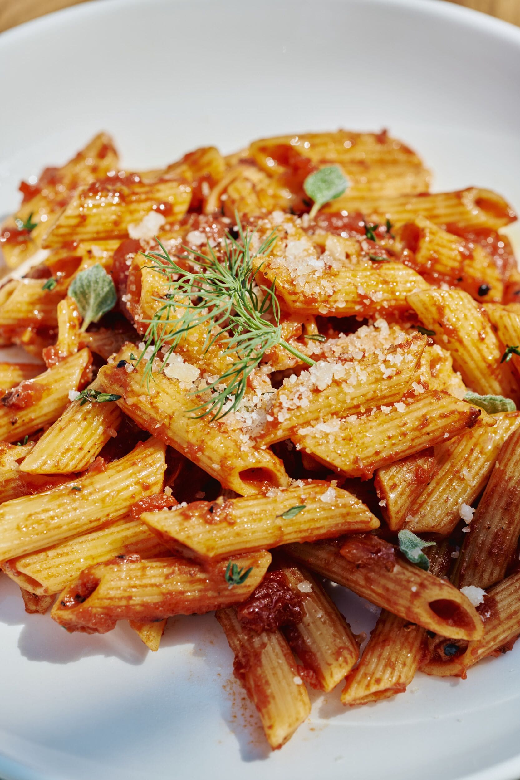 En tallerken med penne pasta, tomatsovs, krydderurter og revet ost.