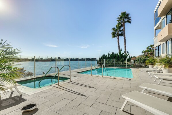 A pool area with two swimming pools, lounge chairs, and palm trees. - Waterfront Condo w/ Dock Access in Carlsbad! (Carlsbad)