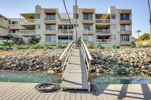 A wooden deck leading to a pool with a backdrop of a multi-story building with balconies and an American flag. - Waterfront Condo w/ Dock Access in Carlsbad! (Carlsbad)