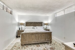 A bedroom with a wooden bed, two bedside tables with lamps, a patterned rug, and a white ceiling. - Waterfront Condo w/ Dock Access in Carlsbad! (Carlsbad)