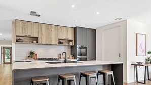 Una cocina moderna con armarios de madera, una isla central con taburetes, horno empotrado y pileta de acero inoxidable.