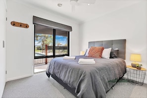 A modern bedroom with a large bed, a nightstand, a lamp, and a view of the outdoors.