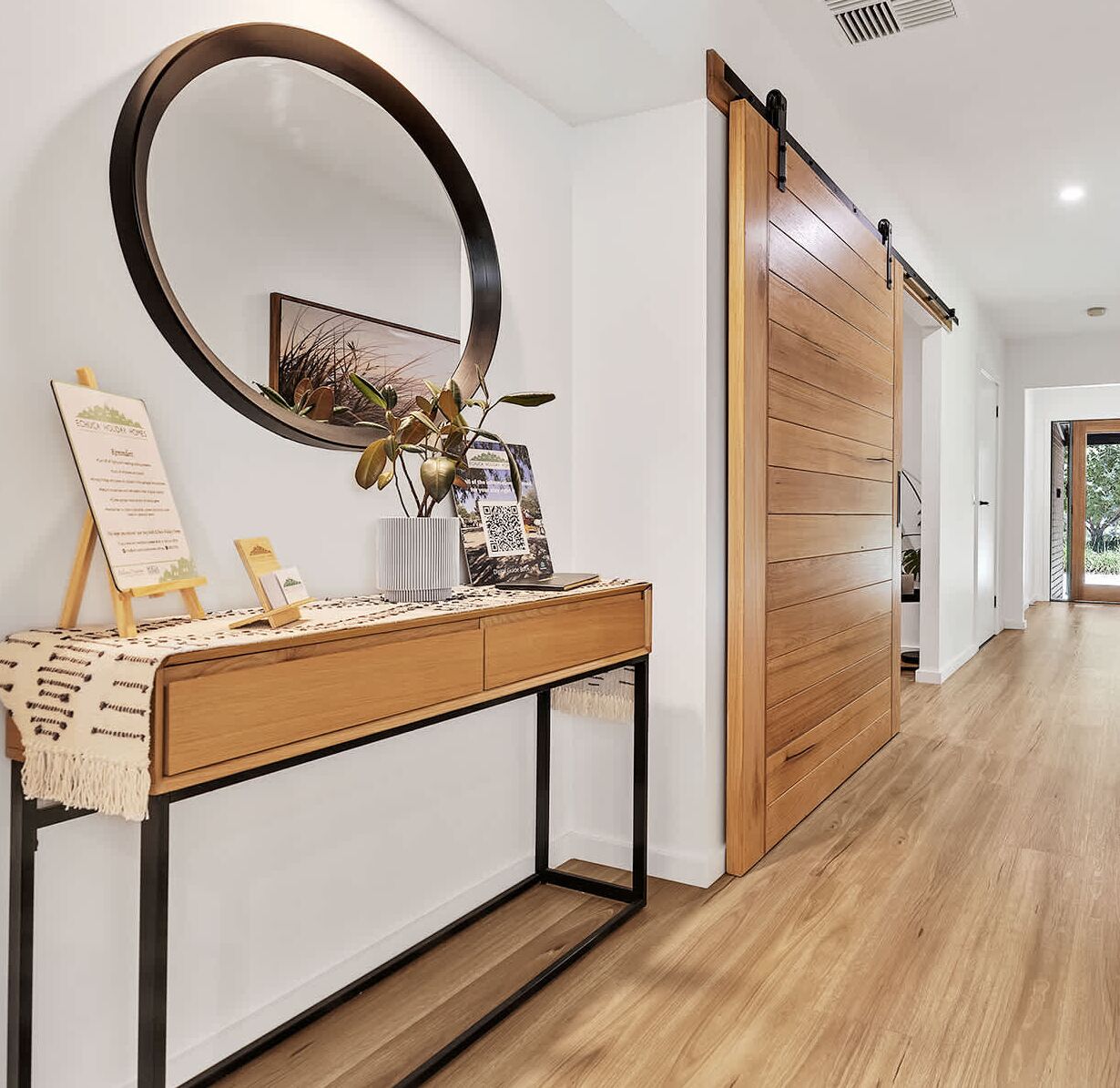 A modern interior with a wooden console table, a large round mirror, and a sliding door.