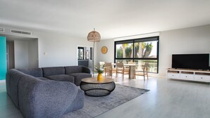 Ein modernes Wohnzimmer mit einem grauen Ecksofa, einem runden Couchtisch und einem Fernseher auf einem weißen Schrank.