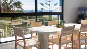 Ein moderner Essbereich mit einem runden Tisch und sechs gewobenen Stühlen, der einen schönen Blick auf Palmen und das Meer bietet.
