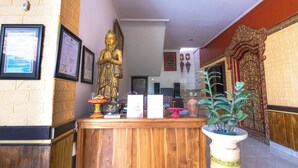 A reception area with a wooden counter, a large golden statue, framed certificates, a potted plant, and a decorative door. - Apartment Kak Okoh  (Munggu)