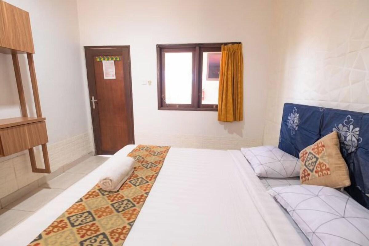 Une chambre d’hôtel avec un lit, un bureau en bois, une porte et une fenêtre avec des rideaux.