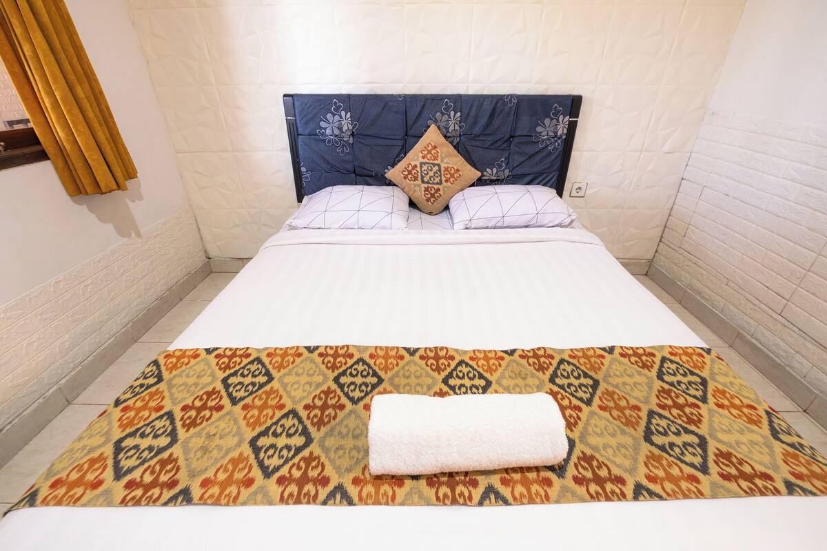 A hotel room with a bed, a patterned bedspread, and a folded white towel on the bed.