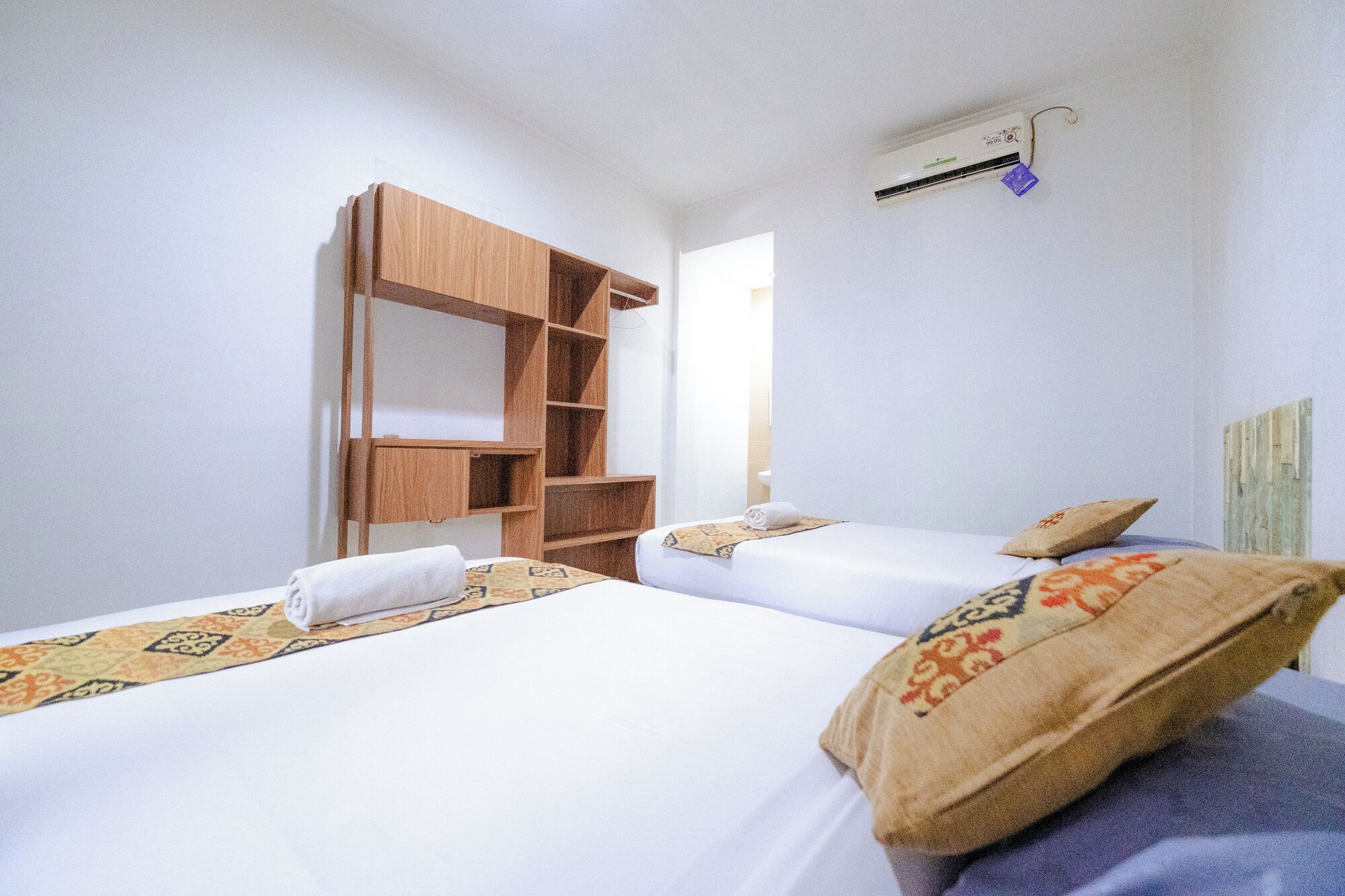 Een kamer met twee bedden, een houten garderobe, een wandairconditioner en een raam.