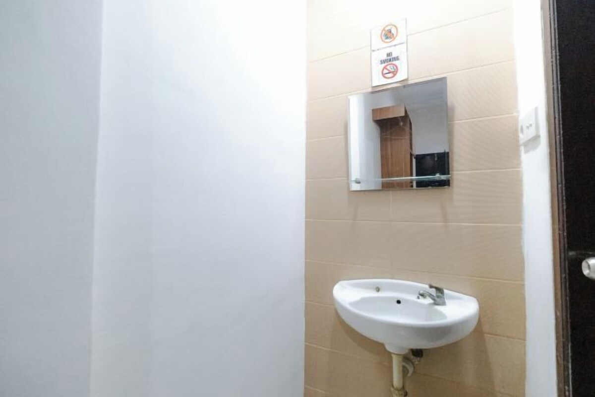 Une salle de bain avec un lavabo blanc, un miroir et un panneau indiquant qu'il est interdit de fumer.