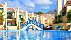 Ein Swimmingpool mit einer blauen Treppe, die zu einem Gebäude führt, umgeben von Palmen und einer Bergkulisse.