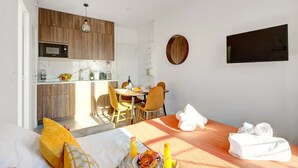Een compacte hotelkamer met kitchenette, eethoek en een bed met handdoeken.