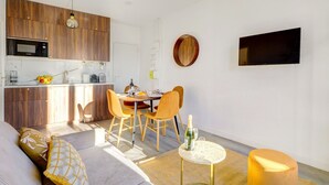 Een modern appartement met een keuken, een eetgedeelte en een woonkamer. Het heeft een bank, stoelen, een kleine tafel en een aan de muur bevestigde televisie.