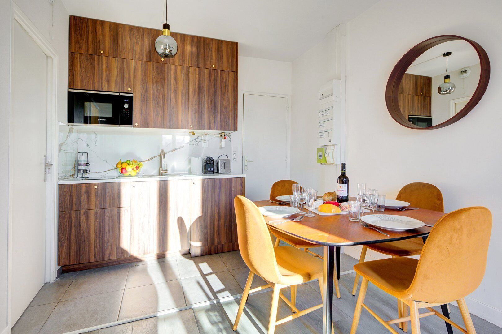 Una cocina moderna con armarios de madera, microondas integrado y una zona de comedor con mesa redonda y sillas amarillas.