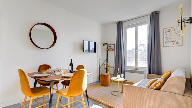 Een moderne woonkamer met een eethoek, een bank, een ronde spiegel en een televisie aan de muur.