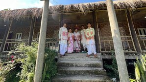 A group of people in traditional attire standing on a staircase in front of a building with a signboard for 'SANGI STAY MAJULI LODGING & FOODING'. - Sarangi Stay By GRB (Majbat)