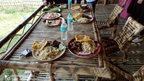 A bamboo table with plates of food, a water bottle, and a camera. - Sarangi Stay By GRB (Majbat)