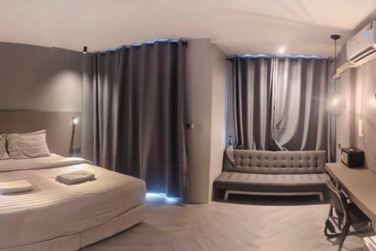 A modern hotel room with a large bed, a sofa, a desk, and a large window.