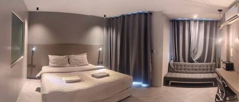A modern hotel room with a large bed, a sofa, a desk, and a large window.