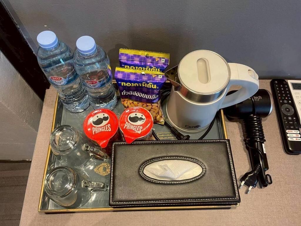 En bakke med vandflasker, Pringles snacks, en kaffemaskine, en fjernbetjening og en strømadapter.