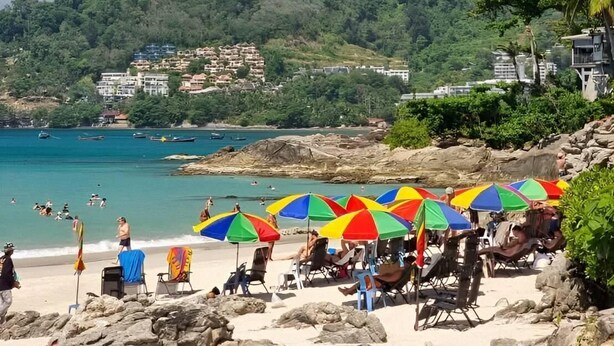 Ein Strand mit bunten Sonnenschirmen und entspannten Menschen.