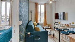 A modern living room with a sofa, a dining area with a table and chairs, a TV mounted on the wall, and a balcony visible through the window. - TBS 141 - Bright and elegant apartment (Paris)