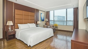 Camera d'albergo con un letto grande, un comodino, una scrivania, una sedia, una lampada, un quadro e un'ampia finestra con vista sugli edifici.
