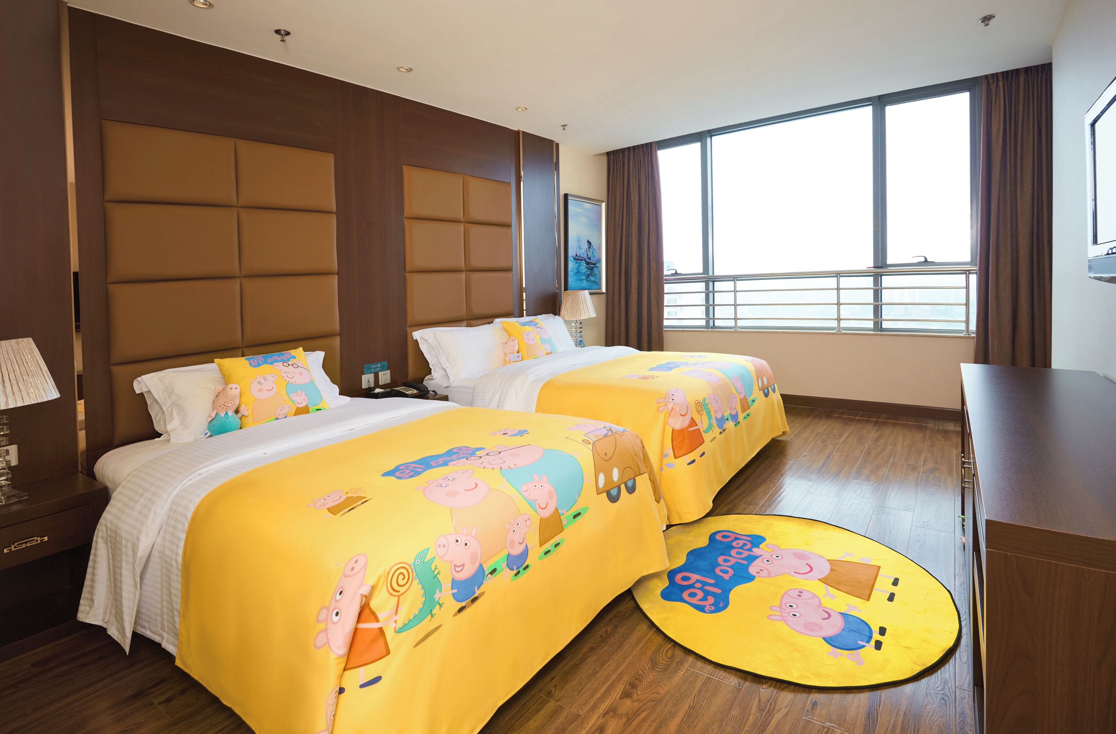 Une chambre d’hôtel avec deux lits, chacun recouvert d’une couvre-lit à motifs de dessins animés, une grande fenêtre avec des rideaux et un plancher en bois.