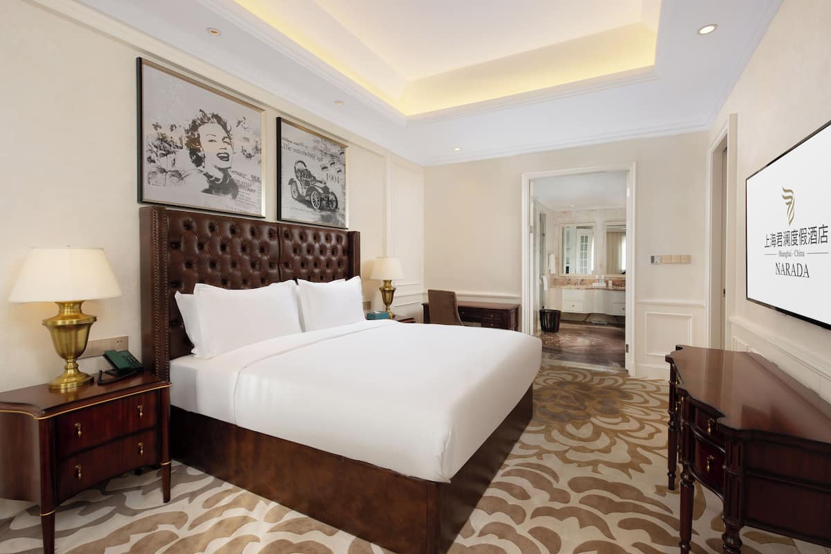 Une chambre d’hôtel avec un grand lit, deux tables de chevet avec des lampes, une tête de lit et des œuvres d’art encadrées accrochées au mur.