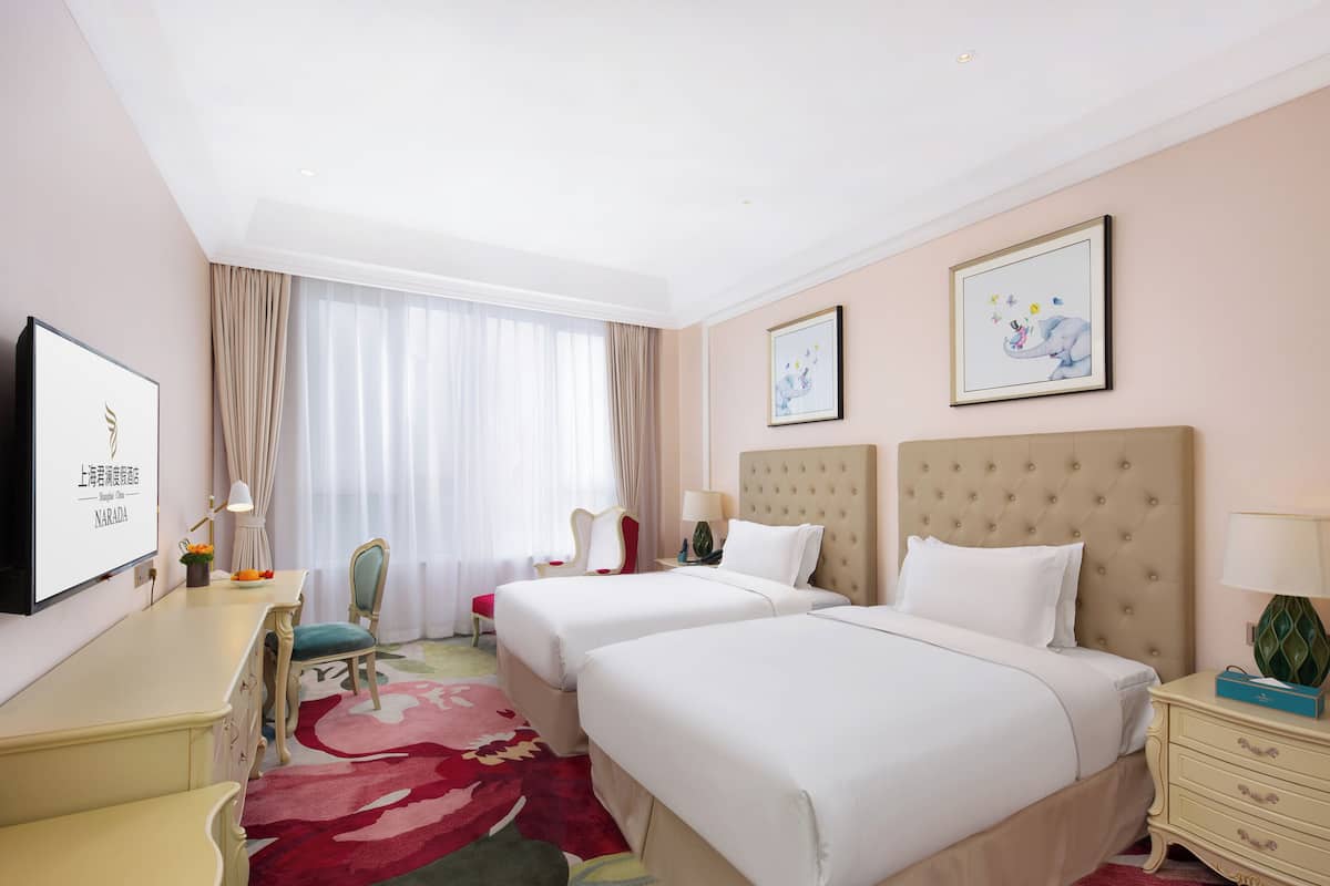 Une chambre d’hôtel avec deux lits, un bureau, une chaise, une télévision et des œuvres d’art accrochées aux murs.