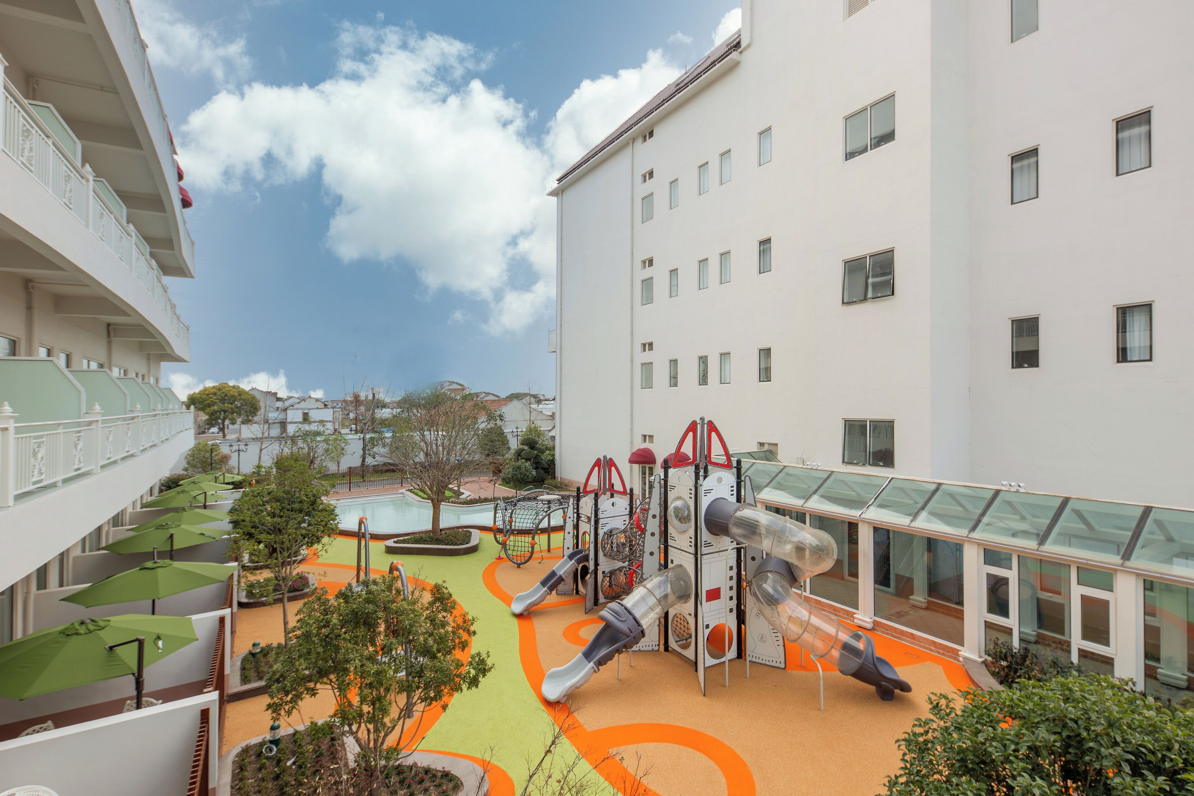 A children's play area with slides and climbing structures, surrounded by a building with balconies and a glass corridor.