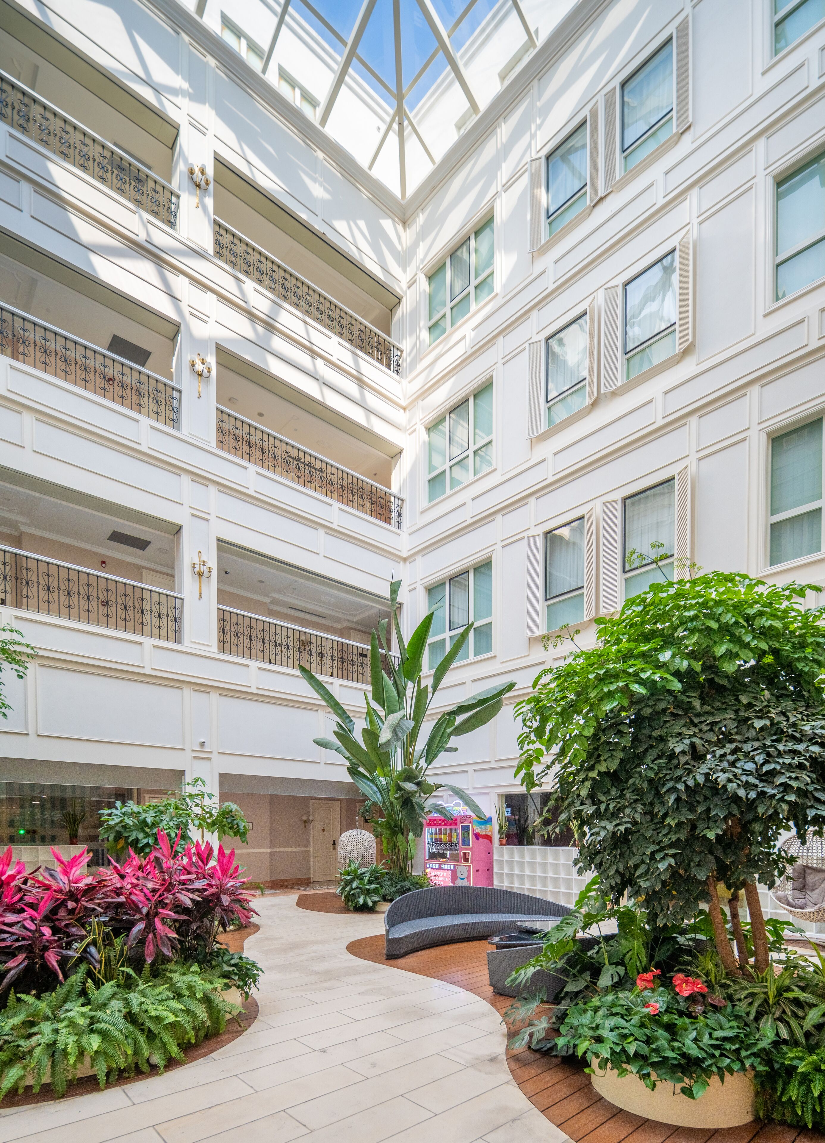 A multi-level atrium with a central walkway, balconies, and indoor plants.