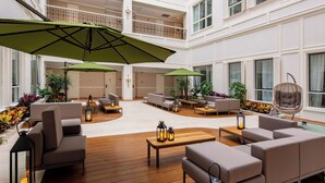 A spacious indoor area with multiple seating arrangements, including sofas and chairs, under large green umbrellas. There are potted plants and a hanging chair visible. - NARADA RESORT SHANGHAI  HOTEL Disney Store (Shanghai)