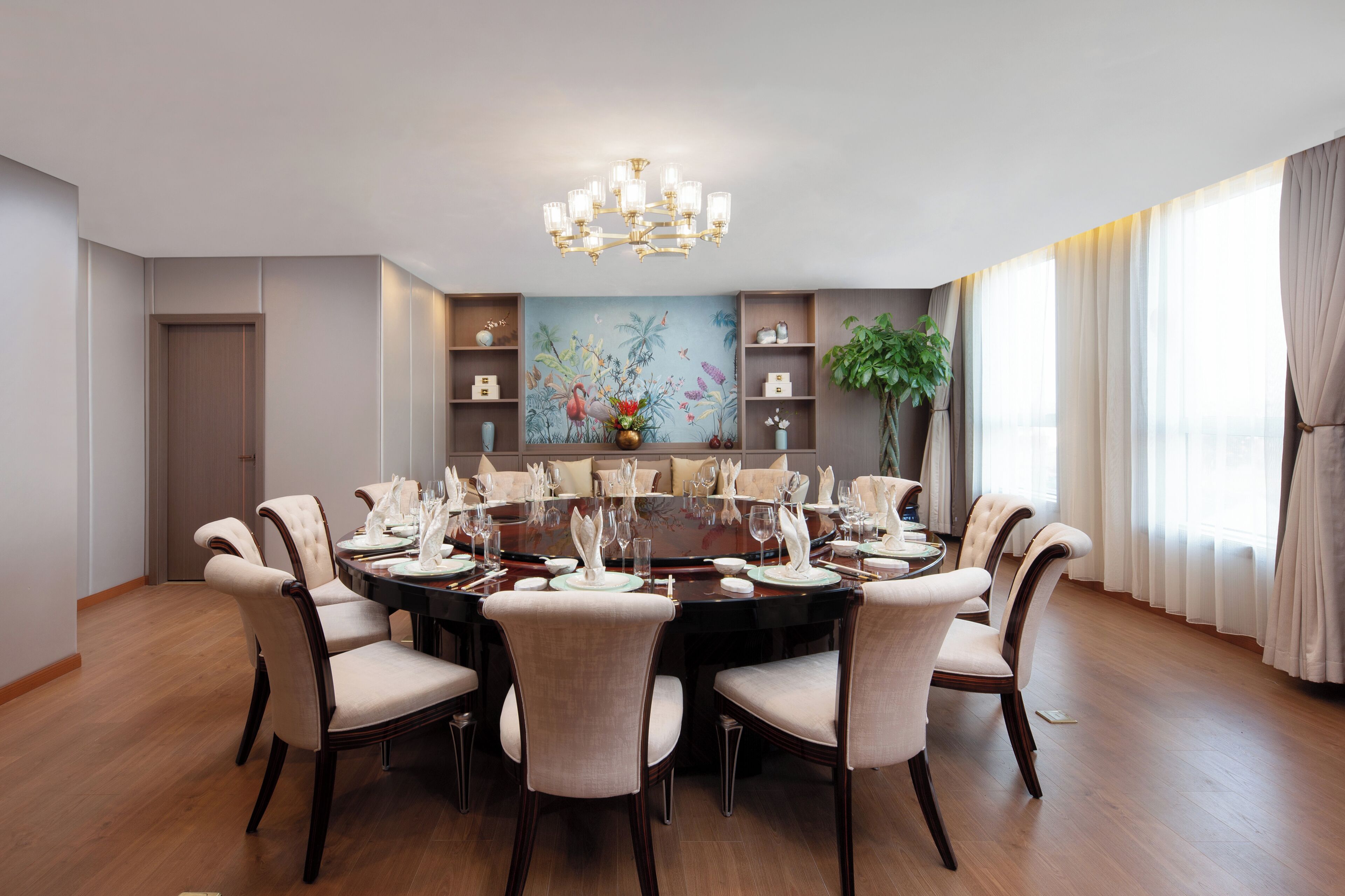 Ein Esszimmer mit einem runden Tisch, gedeckt für acht Personen, umgeben von gepolsterten Stühlen, einer Kristallleuchtre und einem großen Gemälde an der Wand.