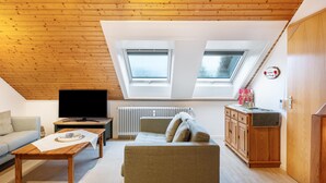 A loft-style room with a wooden ceiling, two skylights, a television, a sofa, a coffee table, and a cabinet.