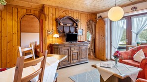 Ein Holzinterieur mit Esstisch, Stühlen, einer Couch, einem Fernseher und einem Schrank.