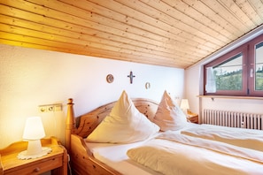 A wooden ceiling, a bed with white bedding, a nightstand with a lamp, and a window with a view.