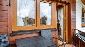 Eine Holzhütte mit Tisch und Stühlen davor, großen Fenstern mit Vorhängen und einer Holztür.