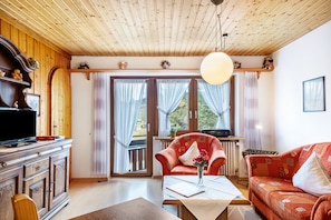A living room with wooden ceiling, a television, a sofa, a chair, and a table with a vase.