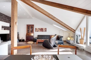 A spacious loft with a high ceiling, exposed wooden beams, a modern kitchen, a living area with a sofa and coffee table, and a dining area with a table and chairs.