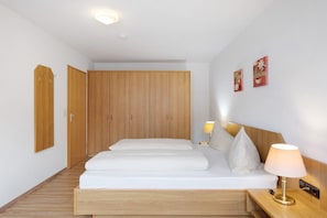 Habitación de hotel con una cama de madera, una mesita de noche con lámpara, un armario y dos cuadros colgados en la pared.