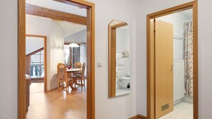 Um corredor com piso de madeira, uma sala de jantar com cadeiras e uma mesa, e um banheiro com vaso sanitário e cortina de chuveiro.