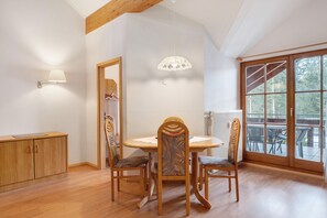 Comedor con mesa y sillas de madera, lámpara colgante y vistas amplias a través de grandes ventanales.
