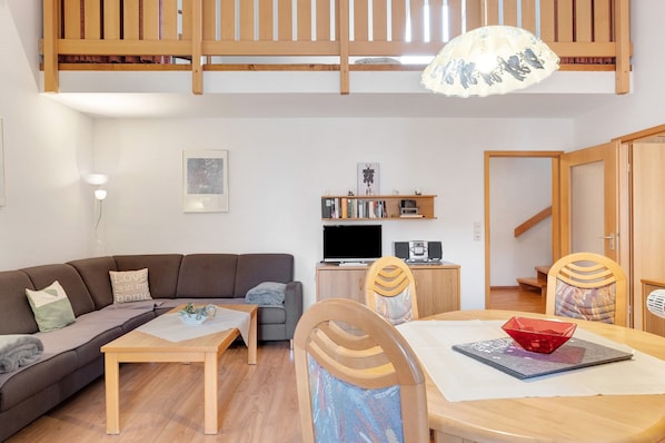 Una sala de estar con sofá, mesa de comedor, sillas, televisor y estantería.