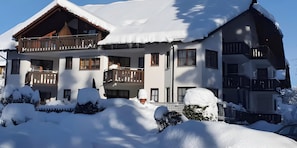 A multi-story chalet with balconies, surrounded by snow-covered ground and trees.