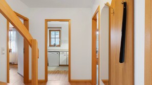 Ein Flur, der zu einer Küche führt, mit einer Holztreppe, einer Tür mit schwarzem Griff und einem Fenster mit Blick.