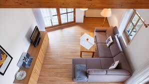 Ein geräumiger Wohnbereich mit einer Couch, Holzboden, einem Fernseher und einem Esstisch.